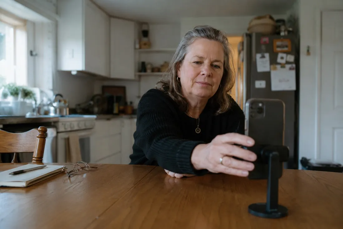 Eine Frau richtet am Küchentisch ihr Handy ein, um sich selbst aufzunehmen.